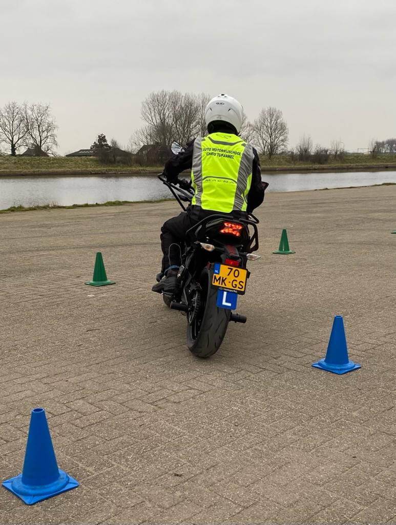 Man op een motor tijdens een motorrijles, met beschermende kleding en helm op een zonnige dag