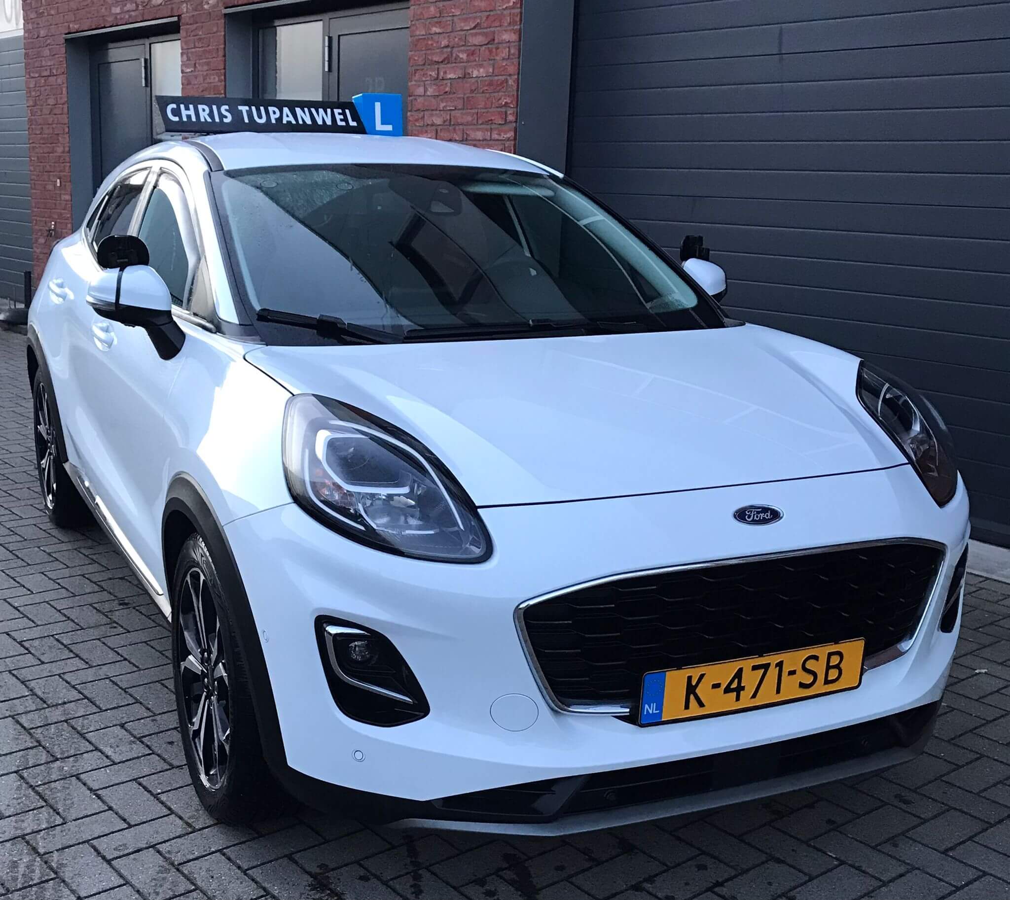 Ford Puma lesauto met een dakbord met opvallende bestickering Chris Tupanwel, geparkeerd in een stedelijke omgeving
